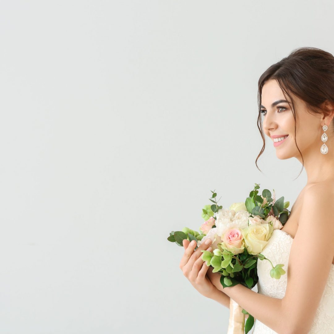 Beautiful young bride with bouquet of flowers on light background